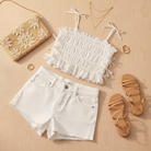 White eyelet tank top flat lay styled with denim shorts, sandals and gold accessories