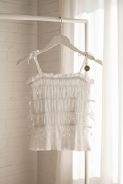 White eyelet tank top with smocked bodice and bow tie straps on hanger with neutral background
